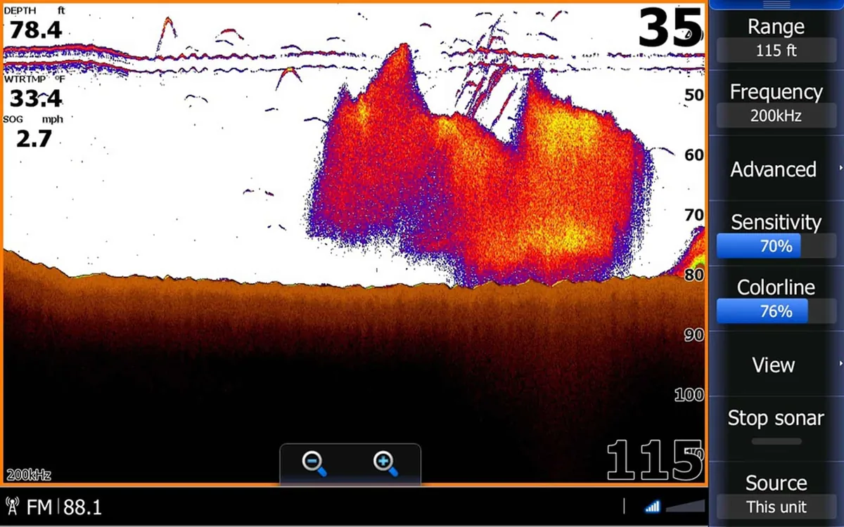 Real Lowrance sonar screen with a huge red and yellow bait cloud above the bottom, small single fish arches around it, and the solid brown bottom band at about 78 feet